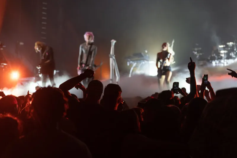 Rock band performs on a smoky stage as a crowd films with phones