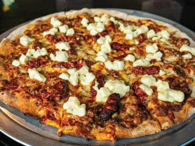 Sliced pizza topped with sun-dried tomatoes, crumbled white cheese, and browned meat on a metal pan