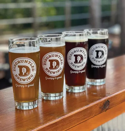 Four Disgruntled Brewing pint glasses ranging from golden to dark amber on a wooden bar