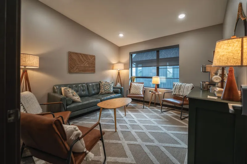 Mid-century modern waiting room with teal leather sofa, brown chairs, and warm lamp lighting