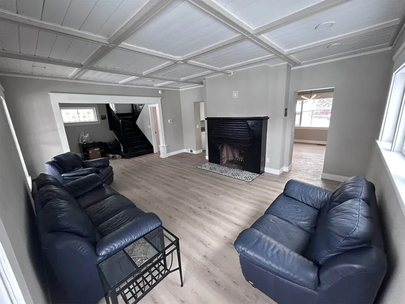 Spacious living room with navy leather sofas, black fireplace, coffered ceiling, and light wood floors