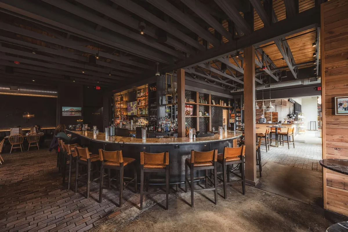 Curved dark bar with stone countertop and wood barstools inside a dimly lit restaurant