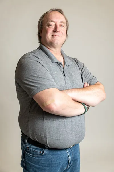 Middle-aged man in a gray polo shirt with arms crossed, smiling at camera