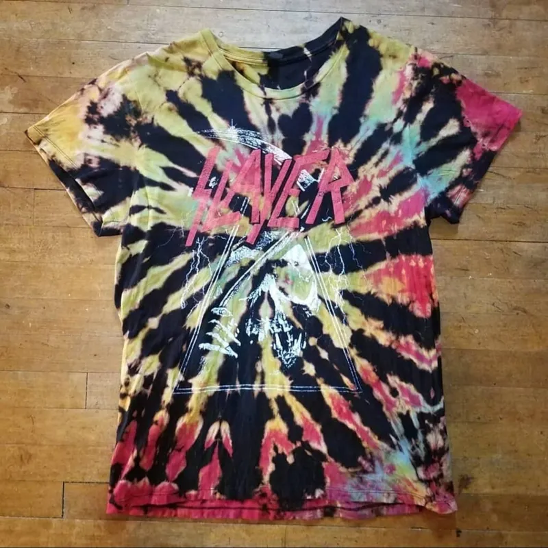 Tie-dye Slayer band tee in swirling black, yellow, red, and teal laid flat on wood floor