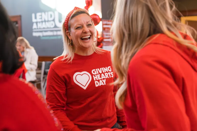 Laughing woman in a red Giving Hearts Day long-sleeve shirt and heart headband at a charity event