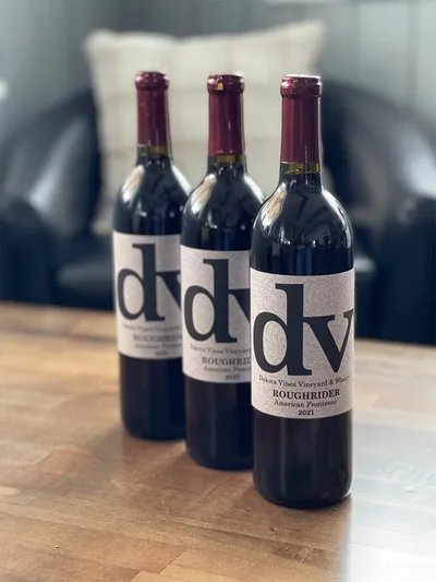 Three bottles of Dakota Vines Roughrider 2021 red wine on a wooden table