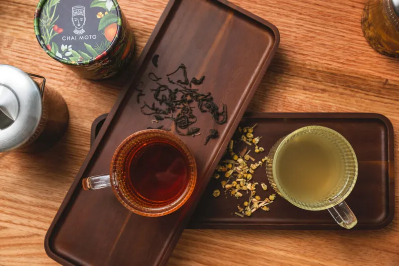 Overhead view of two glass cups of tea on a dark wooden tray with loose-leaf tea and dried flowers