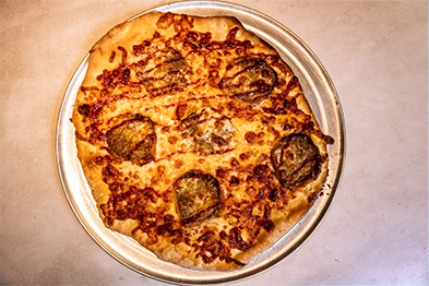 Whole baked pizza with melted cheese and round vegetable toppings on a metal pan