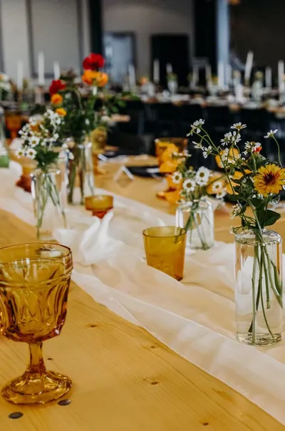Long wooden reception table with wildflower bud vases and amber glassware