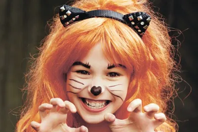 Smiling child with cat face paint, orange wig, and polka-dot cat-ear headband