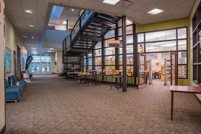 Bright college building interior with open staircase, study tables, and green accent walls