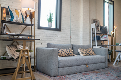 Gray sofa with patterned throw pillows in a furnished studio with white brick walls