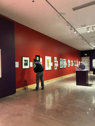 Visitor with backpack viewing framed artwork along a bold red gallery wall