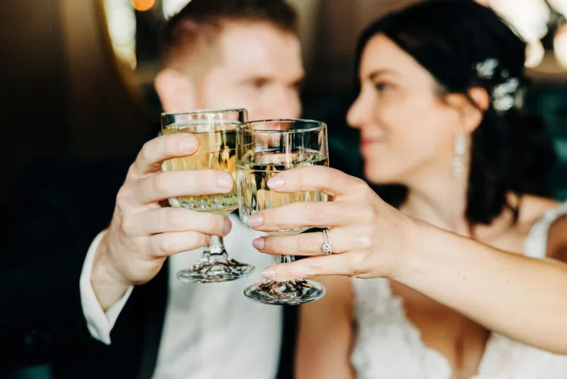 Bride and groom clinking champagne glasses, her diamond ring visible in the foreground