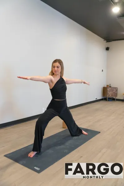 Woman in black activewear holding Warrior II pose on a yoga mat in a bright studio