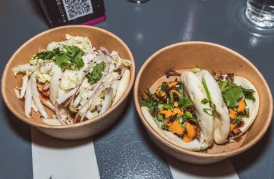 Two kraft bowls — one with a slaw salad, one with steamed bao buns and colorful toppings