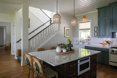 Kitchen island with marble countertop and woven pendant lights beside an open staircase with white balusters