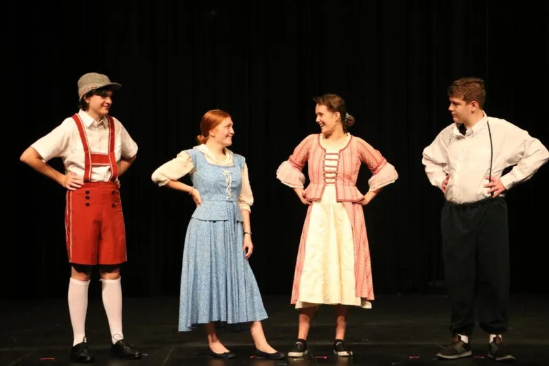 Four teens in period costumes perform on a darkened stage