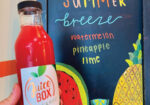 Red juice bottle beside a chalkboard sign reading Summer Breeze with watermelon pineapple lime