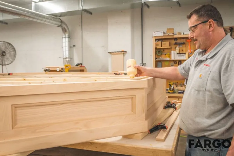 Man in gray polo inspecting a large unfinished wooden cabinet in a workshop
