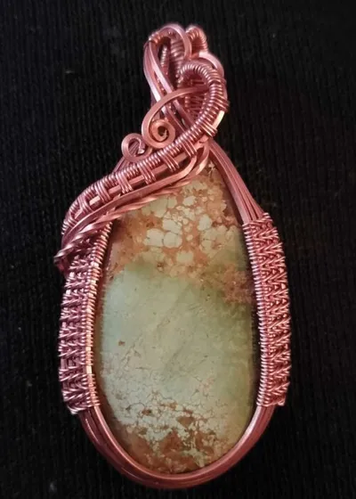 Copper wire-wrapped pendant with a pale green and rust-speckled stone