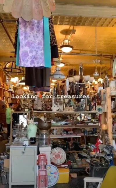 Crowded antique shop interior packed with vintage goods, hanging garments, and pendant lights
