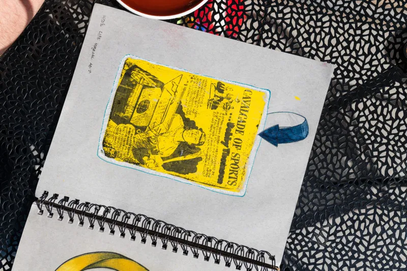 Spiral-bound sketchbook open to a yellow screen-printed 'Cavalcade of Sports' image with a blue arrow