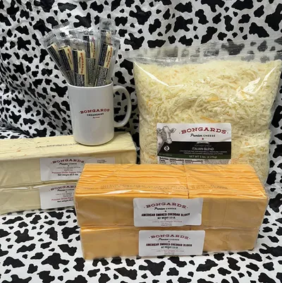 Bongards branded cheese blocks, shredded Italian blend bag, and logo mug with pencils on cow-print surface