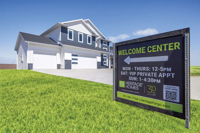 Heritage Homes Welcome Center sign in front of a two-story gray and white house with green lawn