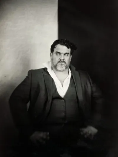 Heavyset man with dark hair and beard in blazer and open-collar shirt, black-and-white portrait