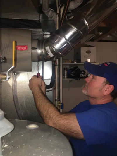 Technician in blue cap inspecting ductwork and pipes on a furnace unit
