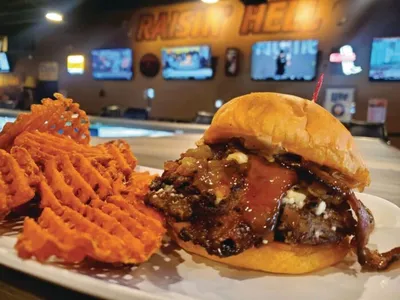 Burger topped with blue cheese and BBQ sauce beside waffle fries on a white plate