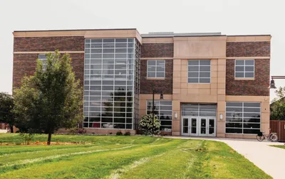 Two-story brick and glass academic building with a green lawn and trees
