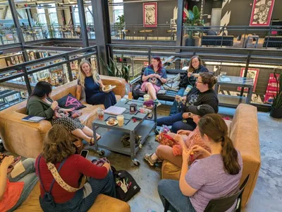Group of women knitting and crocheting together on sofas in a modern open space