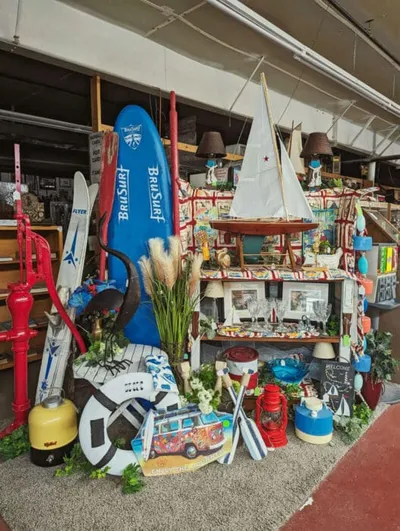 Nautical-themed shop display with surfboards, model sailboats, oars, and coastal décor