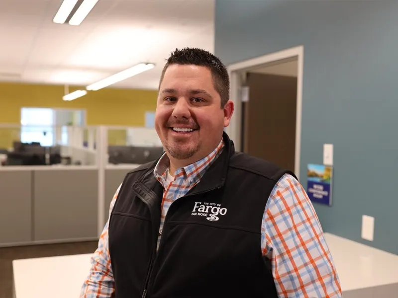 Smiling man in a City of Fargo vest and plaid shirt inside a municipal office