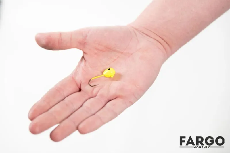 Open palm holding a small yellow jig head with a hook