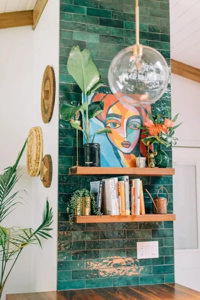 Wooden shelves with books and plants against a green tile wall, with a colorful abstract portrait painting and a glass globe