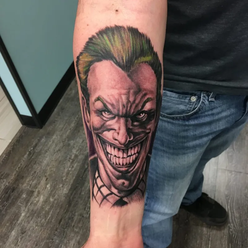Joker character tattoo with green hair and wide grin on a person's forearm