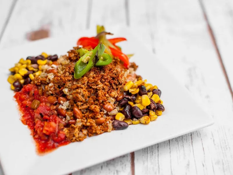 White plate with seasoned ground meat, black beans, corn, salsa, and sliced jalapeños