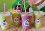 Four colorful drinks in clear cups with straws on a bright counter