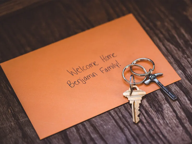 House keys on a keychain resting on an orange envelope reading 'Welcome Home Benjamin Family!
