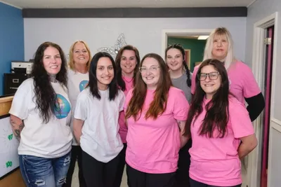 Group of seven women in pink and white T-shirts posing together indoors