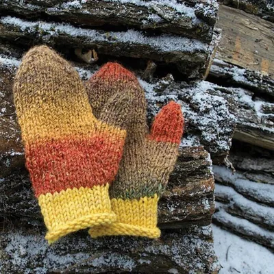 Hand-knitted mittens in yellow, orange, and brown stripes resting on snow-dusted logs