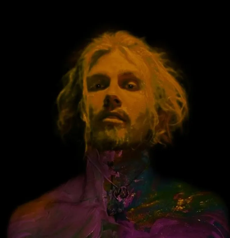 Man with wavy blond hair and beard bathed in warm golden and purple psychedelic lighting