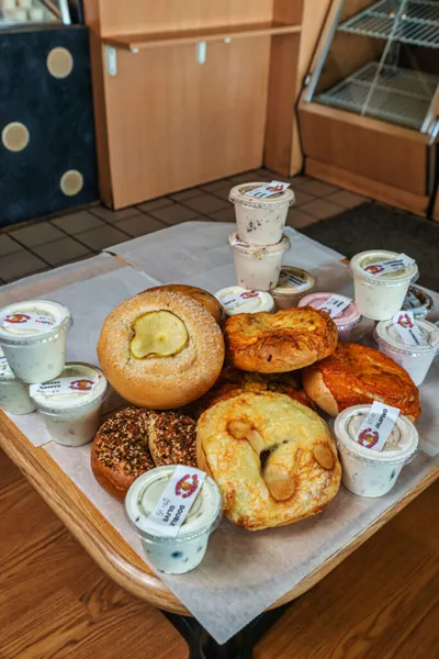 Assortment of bagels and cream cheese cups arranged on parchment paper on a small wooden table