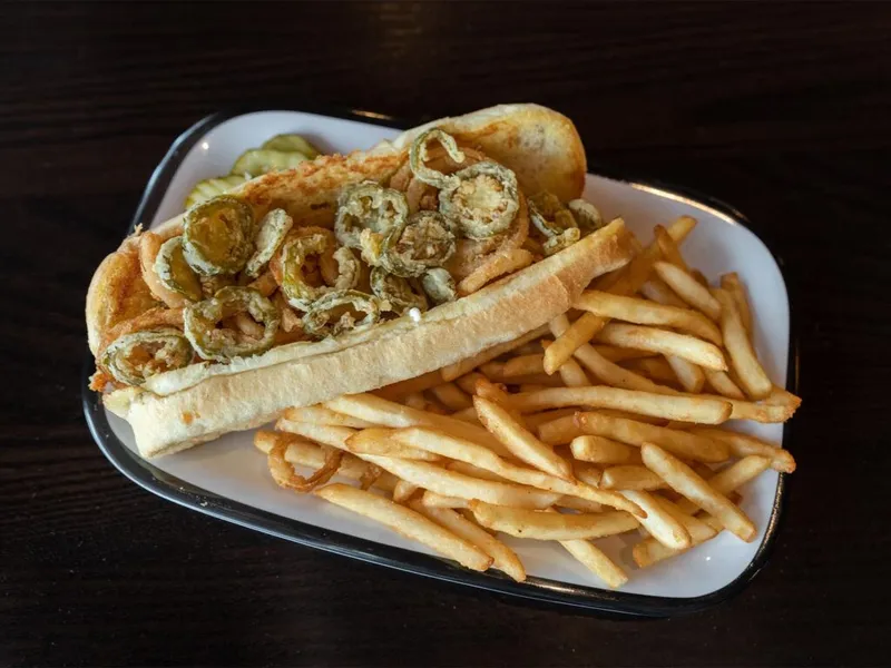 Hot dog topped with fried jalapeño slices on a hoagie bun, served with thin fries on a white tray