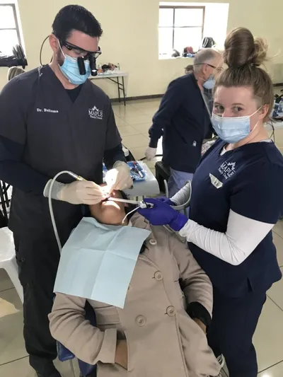 Dentist and dental assistant in scrubs treating a patient at a community clinic