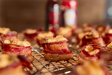 Candied bacon bites on a wire cooling rack with sauce bottles blurred in background