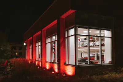 University building lit with red uplighting at night, "Go Dragons" sign glowing inside large windows